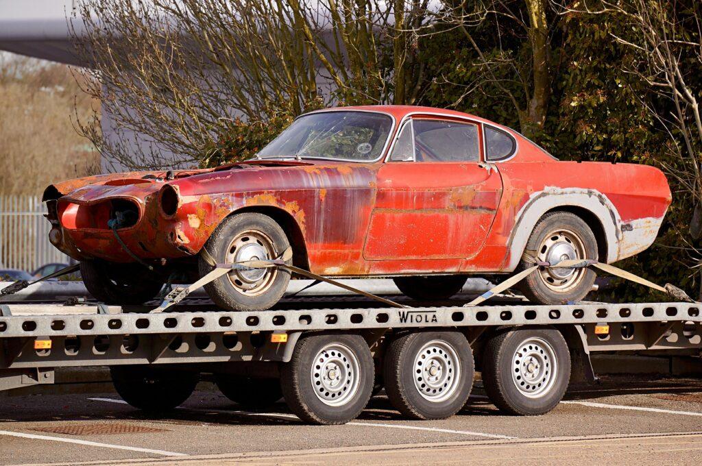 pexels photo 943930 943930 A worn-out, rusty vintage car secured on a flatbed trailer, outdoors under daylight.